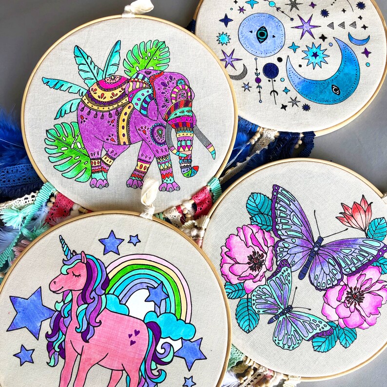 May include: Three embroidery hoops with colorful designs. The first hoop features a purple elephant with intricate patterns, the second hoop has a blue and white moon and stars design, and the third hoop has a purple butterfly and flowers.