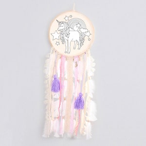 May include: A white wooden dreamcatcher with a black and white outline of a unicorn, rainbow, and stars. The dreamcatcher has white, pink, and purple feathers and tassels.