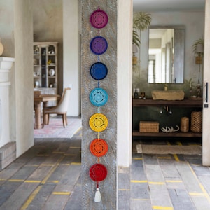 May include: A wall hanging with seven crocheted circles in rainbow colors, hanging from a wooden beam. The circles are connected by a string and have a tassel at the bottom.