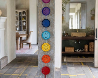 May include: A wall hanging with seven crocheted circles in rainbow colors, hanging from a wooden beam. The circles are connected by a string and have a tassel at the bottom.