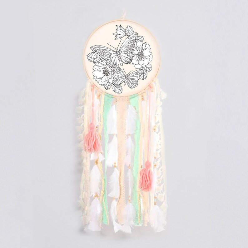 May include: A white dream catcher with a wooden hoop featuring a black and white line drawing of butterflies and flowers. The dream catcher has pink and green ribbons and white feathers.