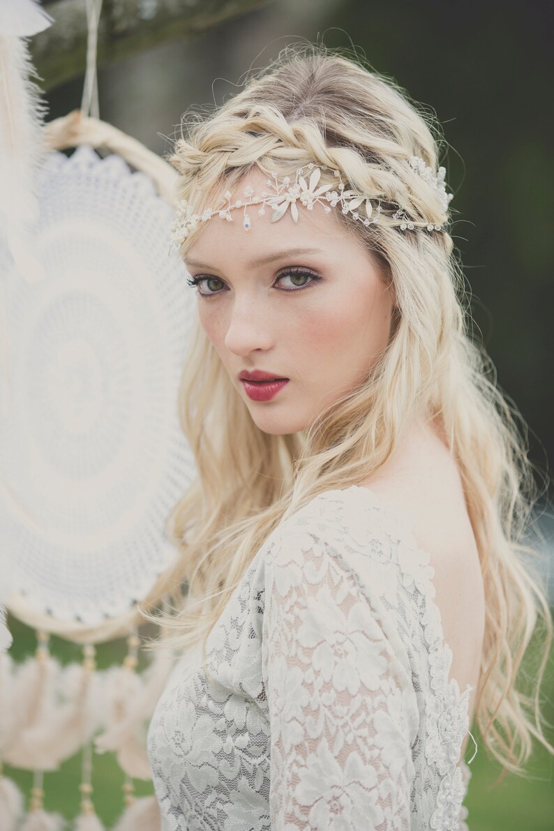 May include: A woman with long blonde hair wearing a white lace dress and a silver headband with rhinestones. She is looking at the camera with a soft smile.