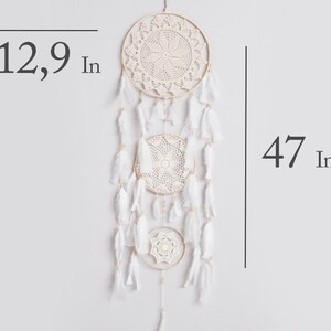 May include: White dream catcher with three circular crocheted hoops and white feathers hanging from the bottom. The dream catcher is 47 inches long and the largest hoop is 12.9 inches in diameter.