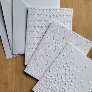 May include: Five white cards with embossed heart patterns. The cards are of different sizes and feature various heart designs.