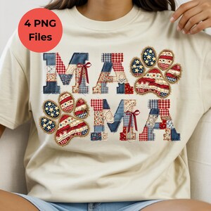 May include: A cream-colored t-shirt featuring the word MAMA in a patchwork quilt style with red, white, and blue patterns, including stars and gingham. Two paw prints are integrated into the design, and small red bows are attached to the letters.