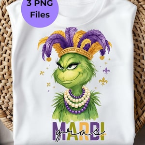 Puede incluir: Camiseta blanca con un personaje de dibujos animados verde con una corona de plumas y un collar de perlas. El personaje sonríe y las palabras "MARDI GRAS" están escritas en morado y dorado. Un círculo morado con el texto "3 PNG Files" está en la parte superior izquierda.