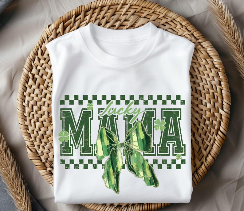 Peut inclure: T-shirt blanc avec un motif de n&oelig;ud vert et blanc et le texte "Lucky MAMA". Le design comprend des tr&egrave;fles verts et une bordure &agrave; carreaux, parfait pour la Saint-Patrick.