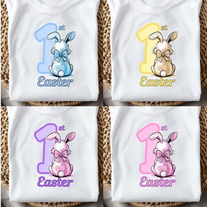 Könnte beinhalten: Weiße T-Shirts mit Ostermotiven. Jedes Shirt zeigt eine große "1" mit "st" darüber, ein Häschen und das Wort "Easter". Die Farben des Häschens und der Zahl variieren: blau, gelb, lila und rosa.