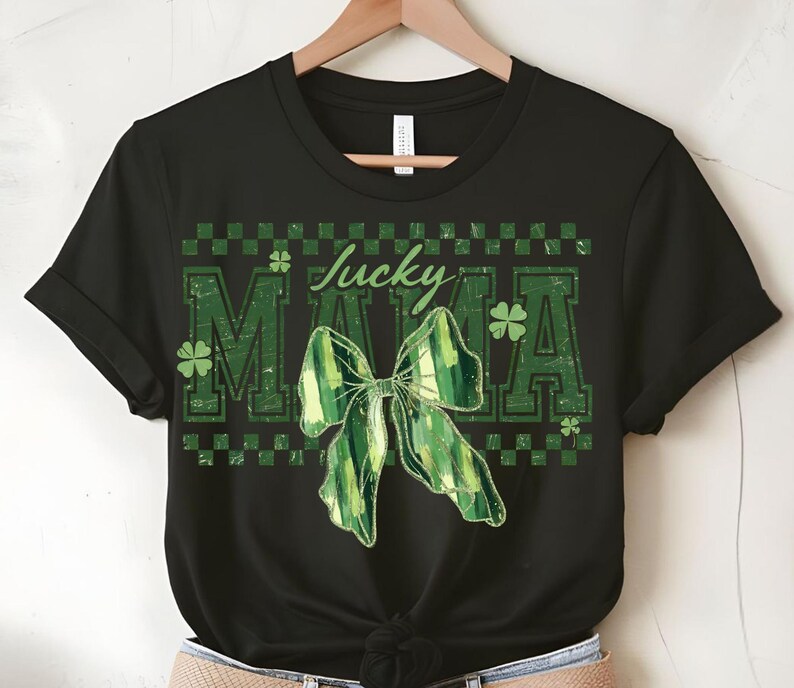 Peut inclure: T-shirt noir avec un motif de n&oelig;ud vert et blanc et les mots "Lucky Mama" en vert. Le motif comprend des tr&egrave;fles et un motif &agrave; carreaux, parfait pour la Saint-Patrick.