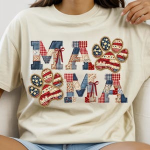 May include: Cream-colored t-shirt with the word "MAMA" in patchwork letters. The letters are made of red, white, and blue patterned fabrics, including gingham, lace, and stars. Paw prints with similar patterns are also featured.