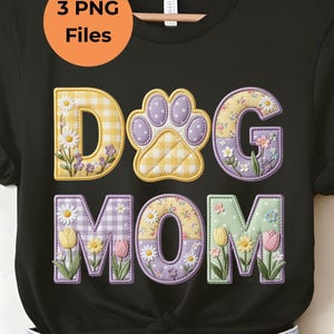 May include: Black t-shirt with the words "DOG MOM" in a floral and patterned design. The letter "D" is yellow gingham, the paw print is purple gingham, and the letters "G" and "M" are floral. The letter "O" is a floral pattern with yellow tulips.