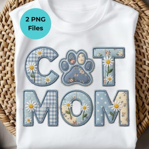 May include: White t-shirt with the words "CAT MOM" in blue patchwork letters. The letters are decorated with daisies and floral patterns. A turquoise circle with the text "2 PNG Files" is in the upper left corner.