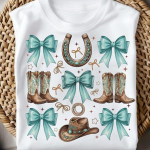 May include: White t-shirt featuring a watercolor design of cowboy boots, a horseshoe, bows, a cowboy hat, and rope details. The design incorporates turquoise and brown colors, with star and bow accents.