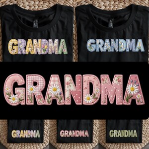 May include: Black t-shirts with the word "GRANDMA" in colorful, floral-patterned letters. The letters have a patchwork design with daisies and other flowers. The shirts are folded on a woven surface.