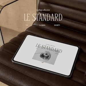 May include: A tablet displaying a digital graphic with the text LE STANDARD, MOCKUP COLLECTION, THE CLOSERS SOCIETY, and a black and white photograph of a tulip. The tablet is resting on a dark brown leather chair with horizontal tufted cushions.
