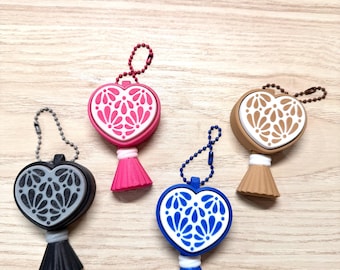Puede incluir: Cuatro llaveros en forma de corazón con cadenas de bolas, cada uno con un patrón floral blanco en el frente. Los llaveros vienen en negro, rosa, azul y bronceado, con una base tipo borla a juego unida a la parte inferior.
