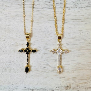 May include: Two gold chain necklaces with cross pendants. One cross is adorned with black cubic zirconia stones, while the other is adorned with clear cubic zirconia stones.