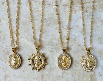 Op de afbeelding: Vier gouden kettingen met verschillende hangers met daarop de afbeelding van de Maagd Maria. Elke hanger is versierd met heldere zirkonia-stenen. De kettingen liggen op een marmeren achtergrond.