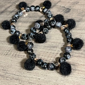 Könnte beinhalten: Zwei schwarze Armbänder mit schwarzen Bommeln. Die Armbänder bestehen aus schwarz-weiß gesprenkelten Perlen.