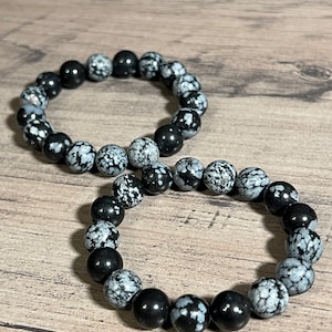 Könnte beinhalten: Zwei Armbänder aus schwarzen und weißen Schneeflocken-Obsidianperlen. Die Armbänder sind übereinander gestapelt.