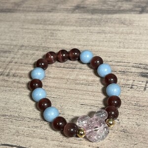 Könnte beinhalten: Ein Armband aus braunen und blauen Perlen mit einem rosafarbenen Kristall-Anhänger in der Mitte.