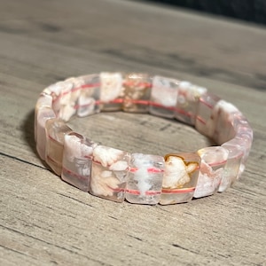 Könnte beinhalten: Ein Armband aus weißen und rosafarbenen Achatperlen mit einer roten und weißen Schnur, die durch die Mitte der Perlen verläuft.