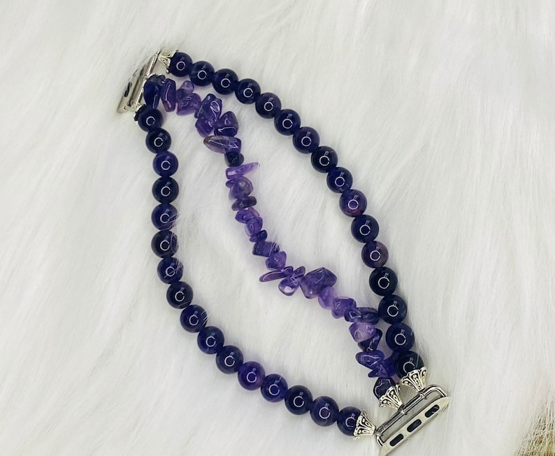 May include: A purple amethyst crystal and black bead Apple Watch band with a silver clasp.