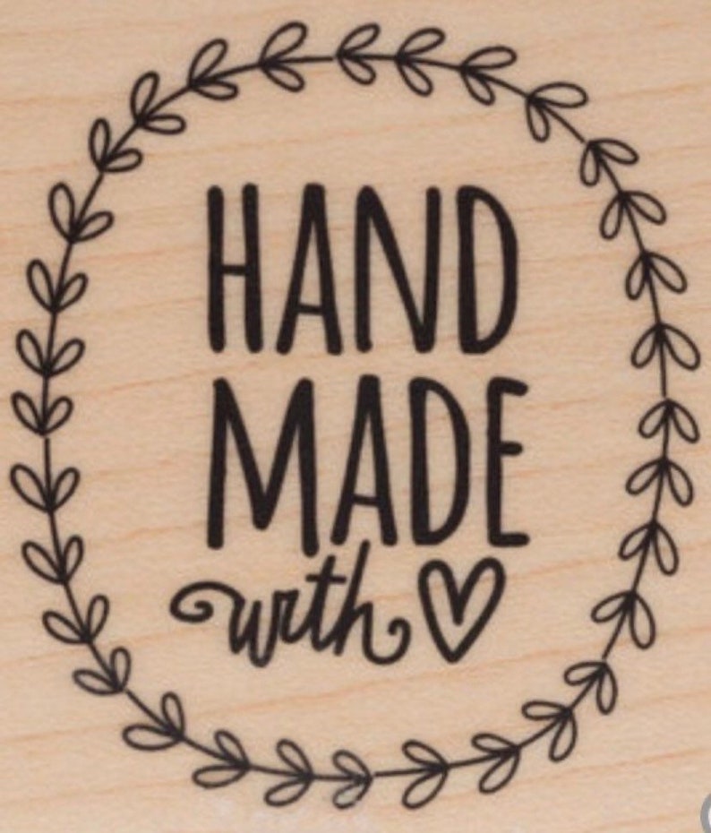 May include: A wooden stamp with a wreath design and the text "HAND MADE with &hearts;".