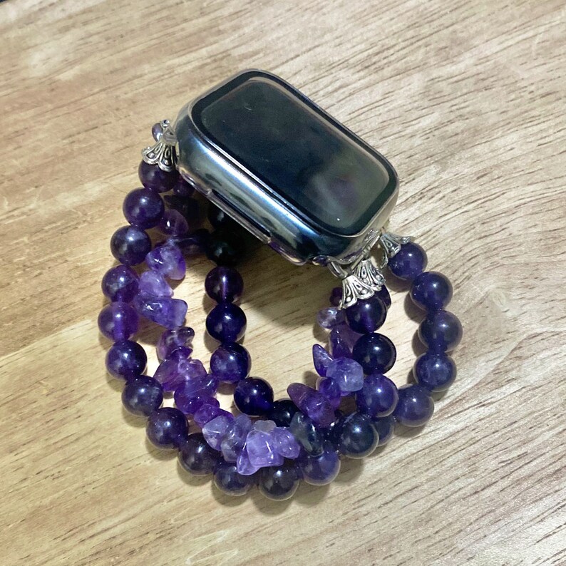 May include: A silver Apple Watch with a purple amethyst beaded band. The band is made of multiple strands of beads, some round and some irregular shaped.