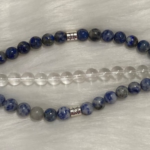 May include: A blue and gray beaded Apple Watch band with silver accents. The band has two rows of beads and a clear crystal row in the middle.