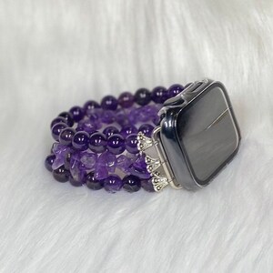 May include: A purple amethyst beaded watch band with a silver clasp and a clear case for an Apple Watch.