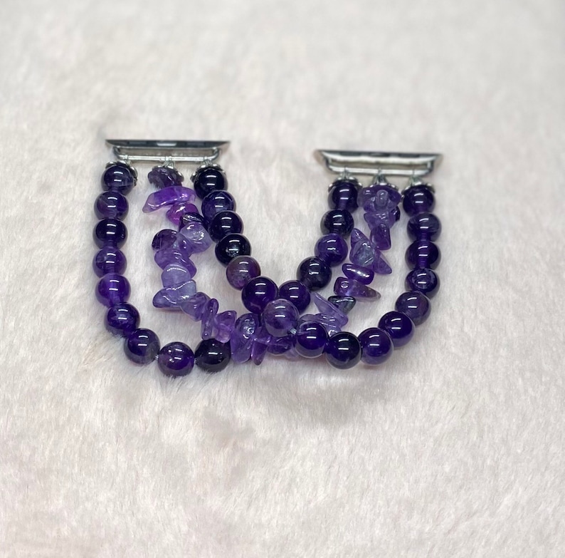 May include: A purple amethyst gemstone bracelet with a silver metal clasp. The bracelet is made of small, round beads and larger, irregular shaped beads. The bracelet is designed to fit an Apple Watch.