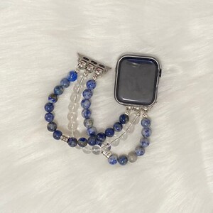 May include: A silver Apple Watch with a blue and white beaded band. The band is made of multiple strands of beads, including blue lapis lazuli and clear quartz.