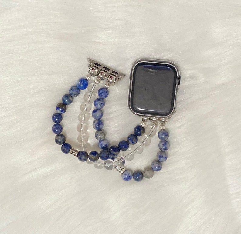 May include: A silver Apple Watch with a blue and white beaded band. The band is made of multiple strands of beads, including blue lapis lazuli and clear quartz.