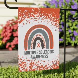 May include: A white garden flag with an orange and gray rainbow design. The rainbow has a small orange ribbon in the center. The text "MULTIPLE SCLEROSIS AWARENESS" is printed below the rainbow.