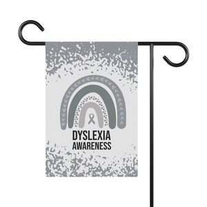 May include: A gray and white garden flag with a rainbow design and the text "Dyslexia Awareness". The rainbow is made up of green, gray, and white stripes. A gray ribbon is in the center of the rainbow.