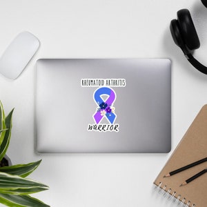 May include: A blue and purple ribbon with flowers, representing rheumatoid arthritis, with the text "Rheumatoid Arthritis Warrior".