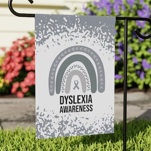 May include: A white garden flag with a gray and white rainbow design and the text "Dyslexia Awareness". The flag is hanging on a black metal flagpole.
