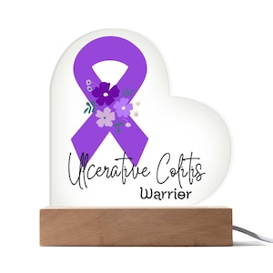 May include: Purple ribbon with floral accents on a white heart-shaped acrylic light base. The base has a wooden stand and the text "Ulcerative Colitis Warrior" is printed on the base.