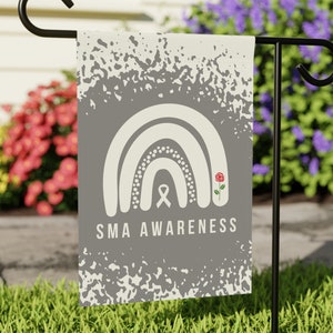 May include: A gray garden flag with a white rainbow, white ribbon, and red rose. The text "SMA AWARENESS" is printed below the rainbow.