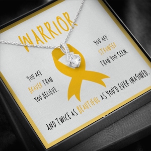 May include: A silver necklace with a yellow ribbon charm and a small clear stone. The necklace comes in a box with a message that reads "You are braver than you believe. You are stronger than you seem. And twice as beautiful as you'd ever imagined."