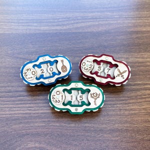 Pode incluir: Três fechaduras de quebra-cabeça de madeira com detalhes coloridos. Cada fechadura apresenta um design único com números e símbolos, incluindo uma guitarra, espadas e uma chave. As fechaduras são pintadas em azul, vermelho e verde.