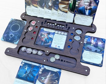 May include: A dark brown wooden game organizer with multiple slots and cutouts for cards, tokens, and dice. The organizer holds various game cards with character illustrations and text. The design includes a central area with a digital display and several small, round tokens.