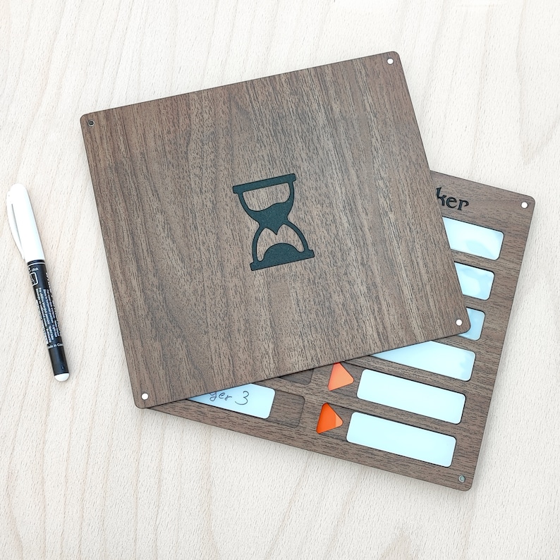 May include: A wooden board game with a dark brown finish, featuring an hourglass symbol and a section with white rectangles and orange triangles. A white marker pen is placed on the left side of the board.