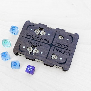 Puede incluir: Un tablero de juego de madera oscura con las palabras "Investiture", "Health", "Focus" y "Deflect". El tablero tiene secciones recortadas con números. Varios dados translúcidos azules, verdes y morados están esparcidos alrededor del tablero.