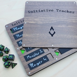 May include: Wooden initiative tracker with the text "Initiative Tracker" and a black symbol. Includes black and green dice and black labels for players and monsters. The tracker is made of wood.