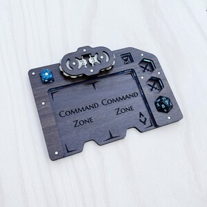 May include: Wooden game board with the words "Command Zone" and dice. The board is dark brown with a lighter brown border and has several cutouts for dice and other game pieces. A blue and white speckled die is on the left side.