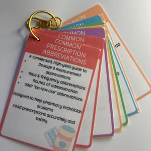 May include: A set of flashcards on a gold keyring, titled "COMMON PRESCRIPTION ABBREVIATIONS." The red card lists abbreviations for dosage, time, and routes of administration. Designed for pharmacy technician students to read prescriptions accurately.