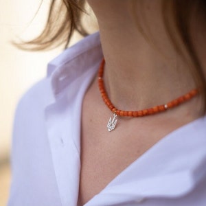 May include: A necklace featuring small, round, orange beads strung together with occasional silver-toned spacers. A silver-toned pendant shaped like the Ukrainian Tryzub emblem hangs from the center of the beaded strand.