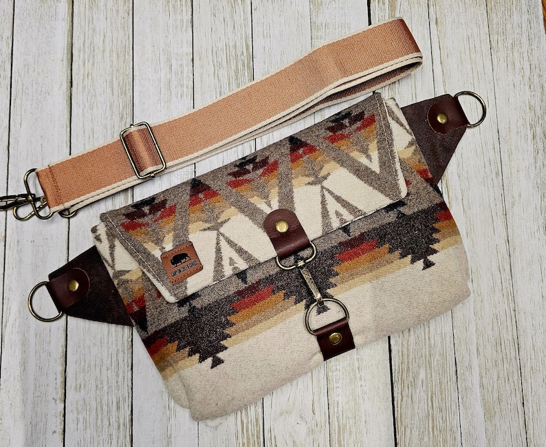 Puede incluir: Ri&ntilde;onera estampada con una correa ajustable de color beige. La bolsa presenta un dise&ntilde;o geom&eacute;trico en tonos marrones, rojos y crema. Tiene detalles de cuero marr&oacute;n y un cierre met&aacute;lico. La correa es beige con herrajes met&aacute;licos.